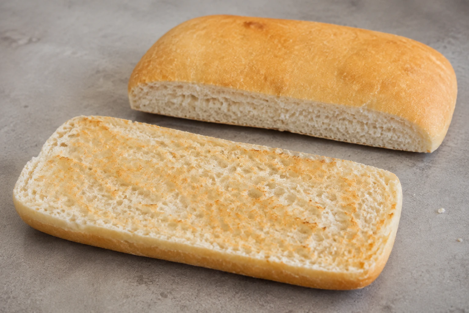 A low rectangular white roll split open, with a lightly toasted cut face and thin golden crust