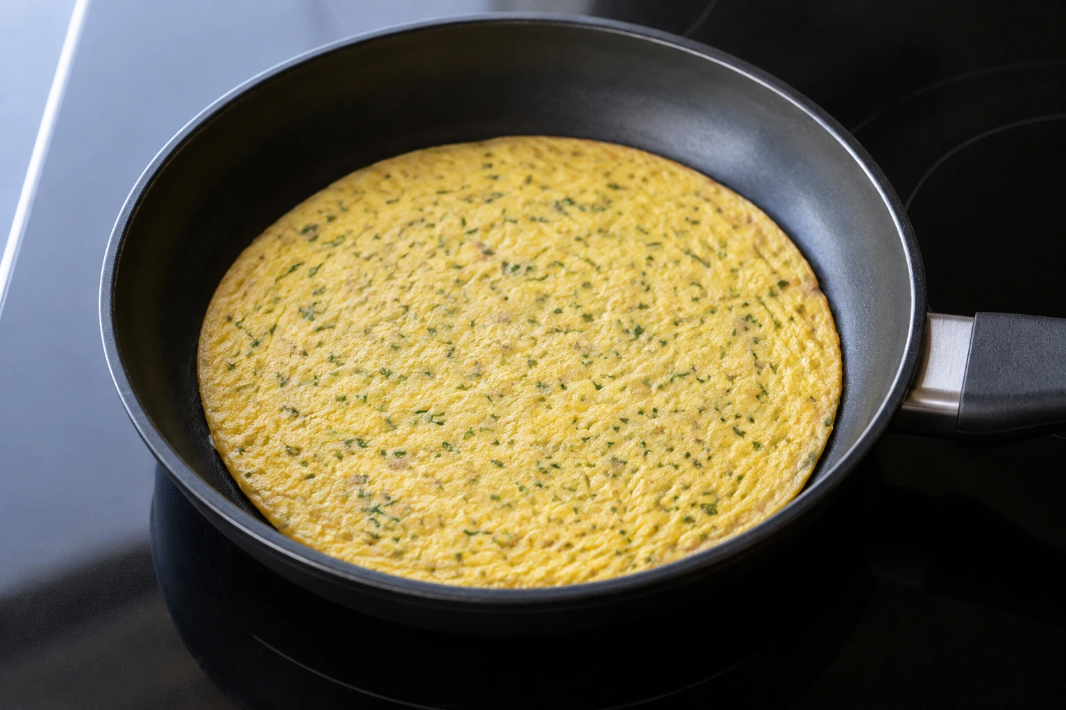An unfolded round of fully set egg with fine shallot and chive flecks in a frying pan