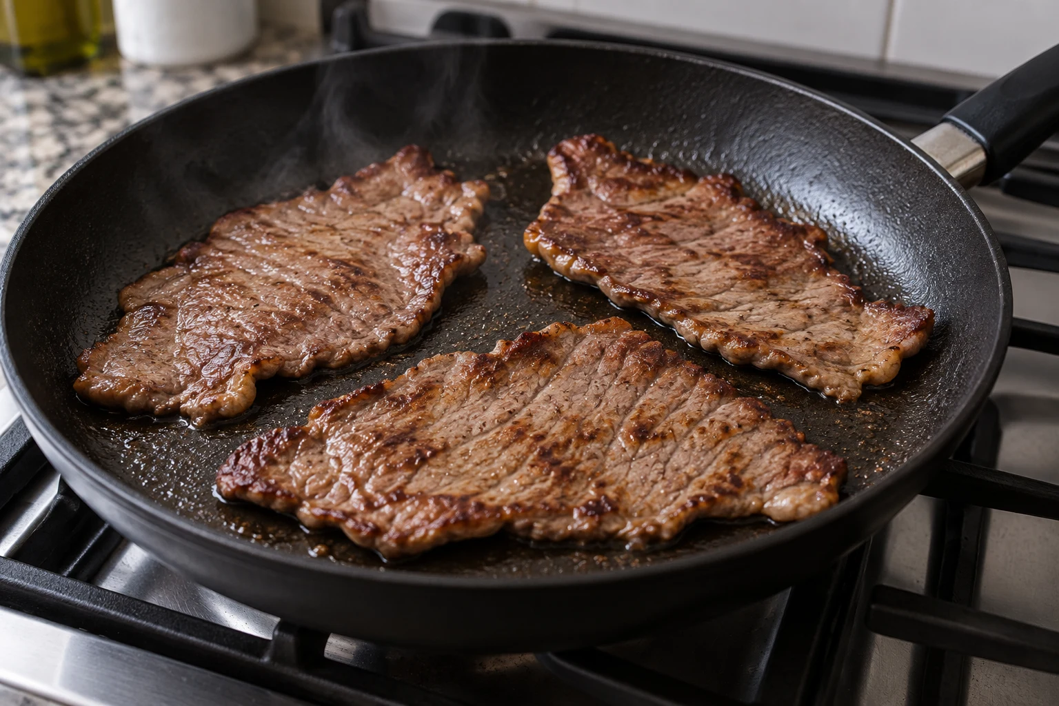 Separate thin whole-muscle beef steaks browning in a skillet with a small amount of oil
