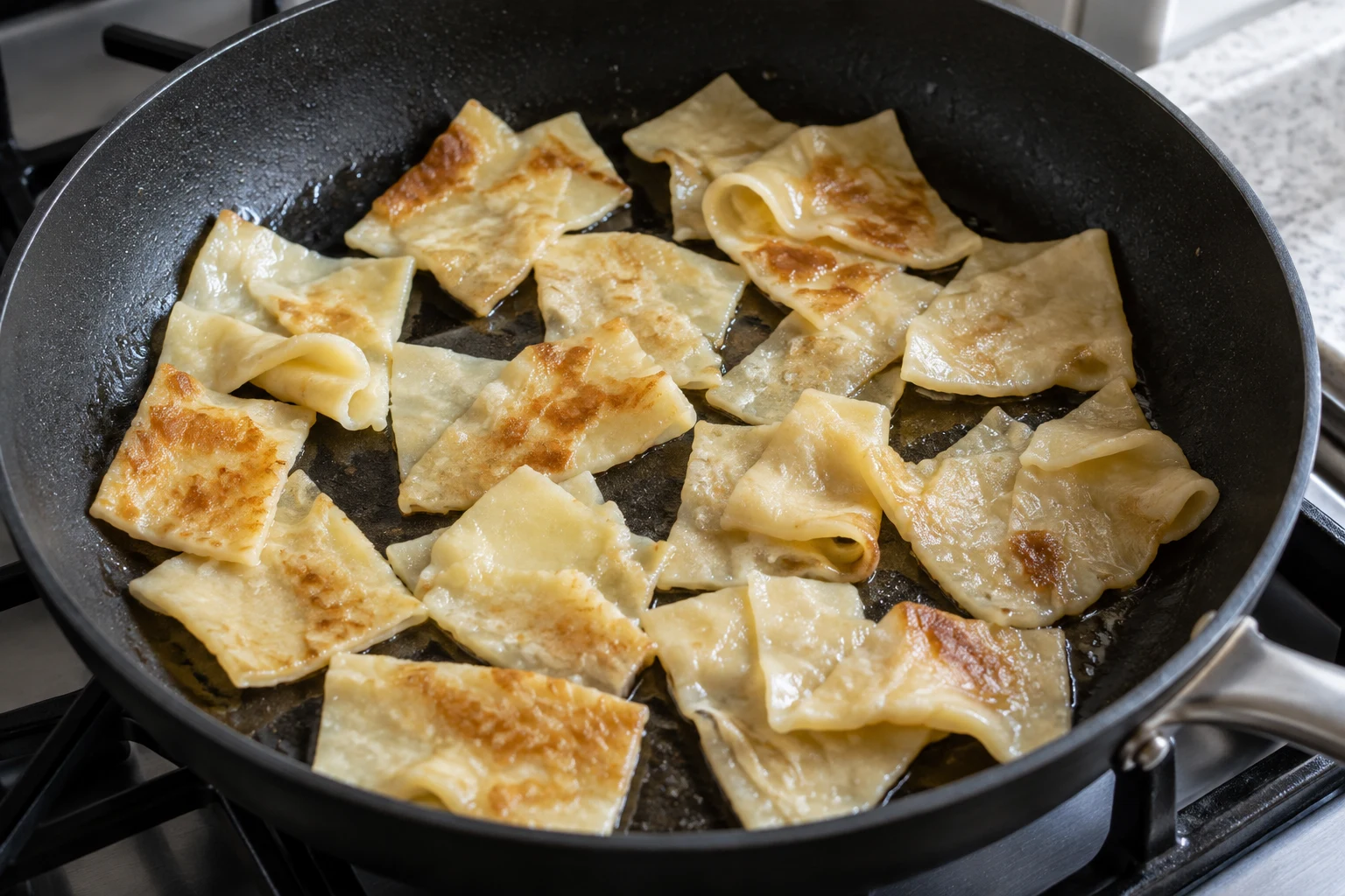 Broad folded pasta pieces with golden-brown patches in a thin sheen of fat in a frying pan