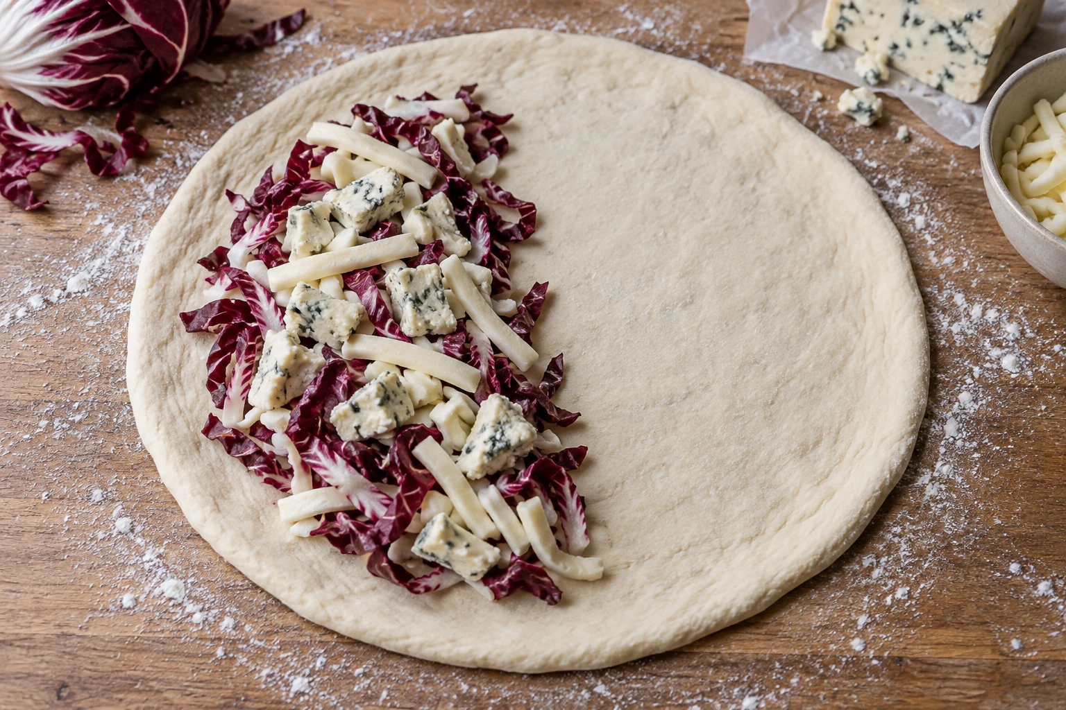 One half of a pizza dough disc holds mozzarella, blue cheese and radicchio while the other half and border remain bare