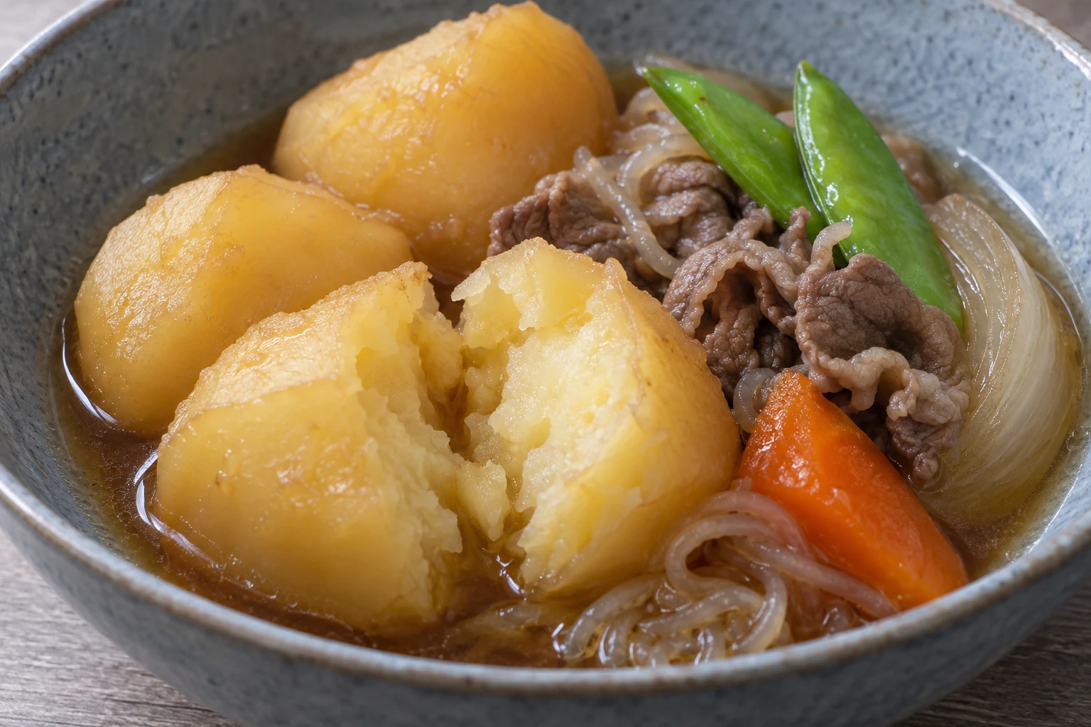 An opened cooked potato chunk beside intact potatoes, thin beef and snow peas in nikujaga