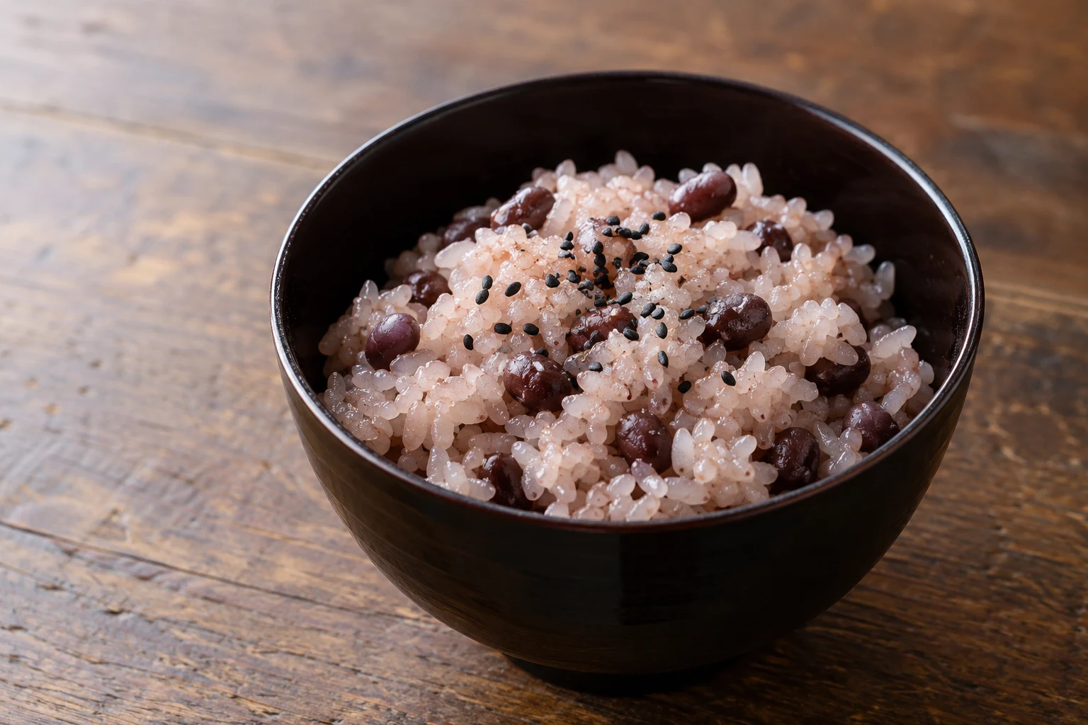 Pink-tinted short-grain sekihan with small maroon azuki beans and black sesame in a dark bowl