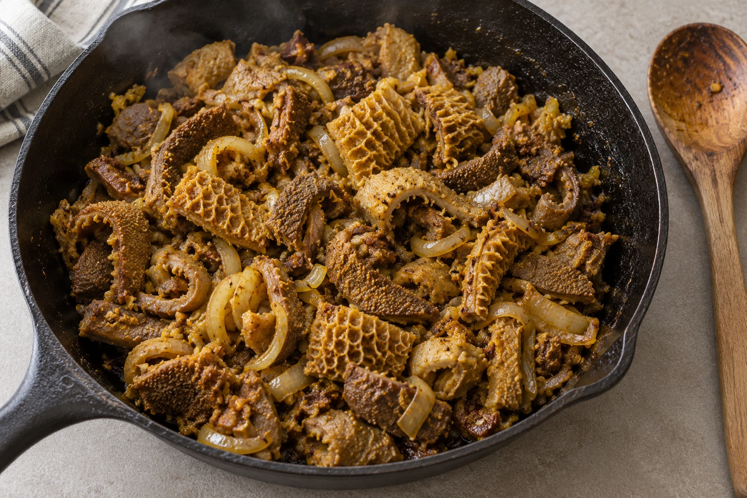 Cooked spiced tripe and golden onion in a black iron skillet
