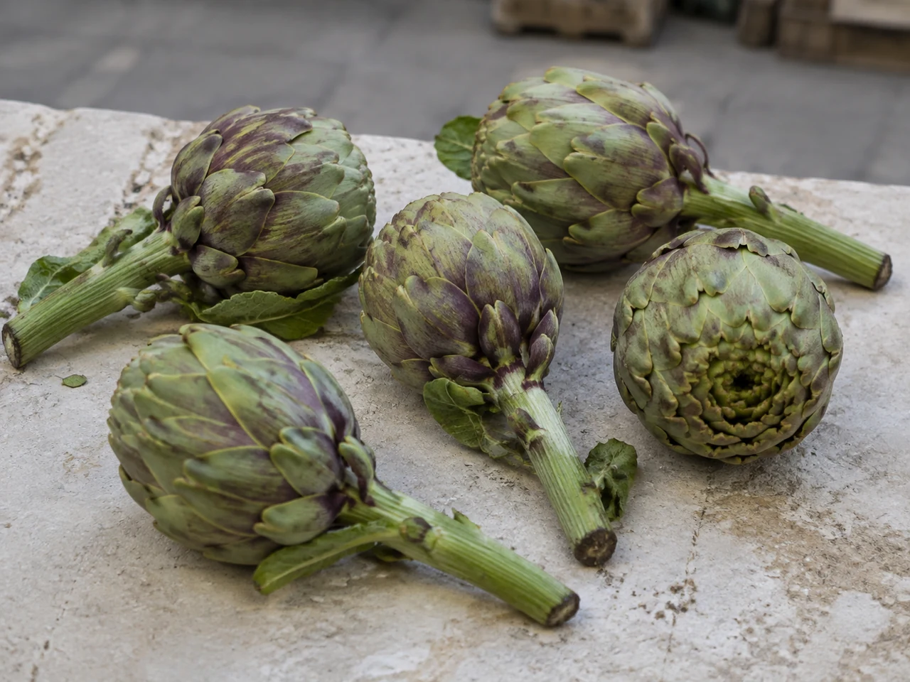 Fresh round green and violet artichokes with long stems on a stone market counter