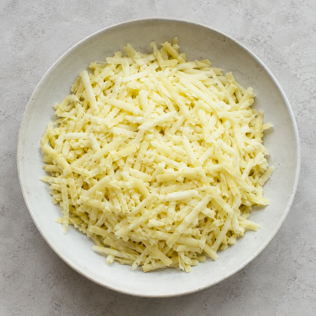 Coarsely grated cooled potatoes in a shallow ceramic bowl